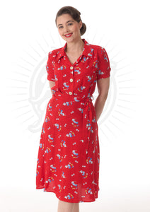 A red dress with small floral patterns on it, with a shirt style bodice that has an open collar and three light buttons down the front, with short sleeves. A matching colour tie belt adorns the waist and the skirt is a slightly flared A line to the knee.